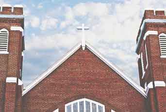 The brick gable and twin towers of a community church building against a partly clouded sky.